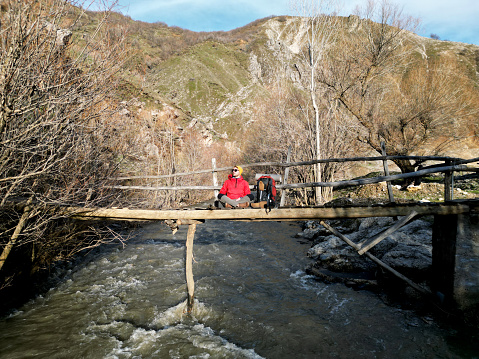 Hiker Man walking along wooden suspension bridge over river