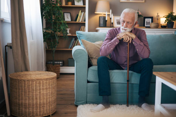 istock Senior man sitting at the sofa holding walking cane. 2120747922