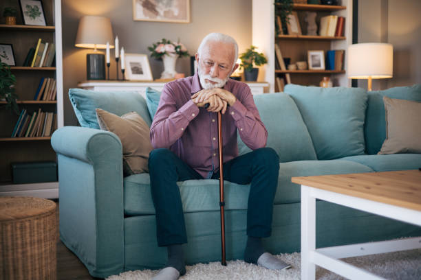 istock Senior man sitting at the sofa holding walking cane. 2120748952