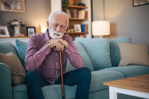 istock Senior man sitting at the sofa holding walking cane 2120749466