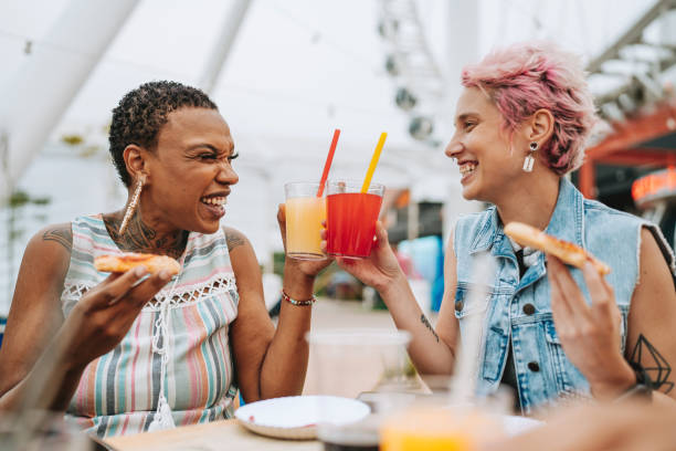 Two friends eating pizza and toasting with drinks