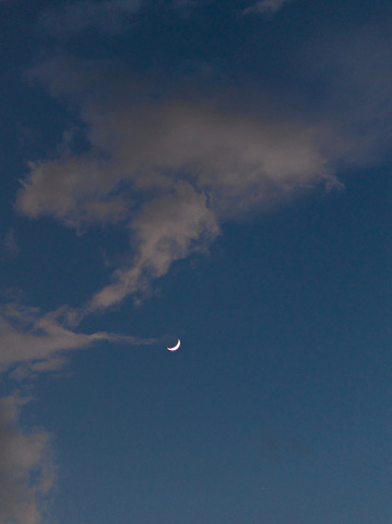 thin clouds beneath a blue twilight sky, enveloping the hidden face of a distant crescent moon - POA,  SAO PAULO,  BRAZIL.