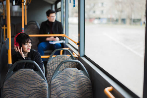 Cheerful young woman looking through the bus window and listening music