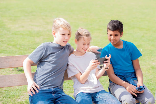 istock teens friends looking at phone while sitting in park 2120797019