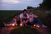 Diversity family of four plays with sparklers on rural path, sharing cozy moment