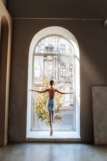 istock Young ballerina stands en pointe, back to the camera, framed by an arched window 2120809618