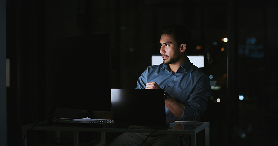 Young man, thinking and computer at night for information technology, programming or cybersecurity solution. Professional programmer or expert with problem solving or ideas on laptop in dark office
