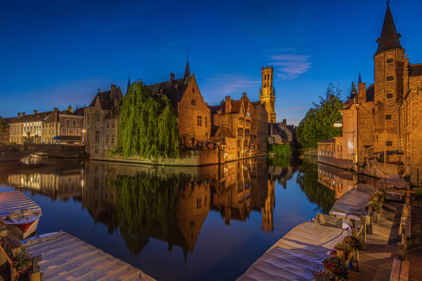 Center of the old town of Bruges with a view of the Rosary Quay. Old Belgian Hanseatic town with canal at blue hour. Reflections of illuminated historic merchant houses and belfry on the water surface