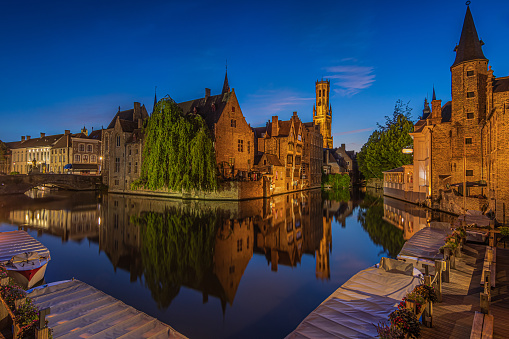 Center of the old town of Bruges with a view of the Rosary Quay. Old Belgian Hanseatic town with canal at blue hour. Reflections of illuminated historic merchant houses and belfry on the water surface