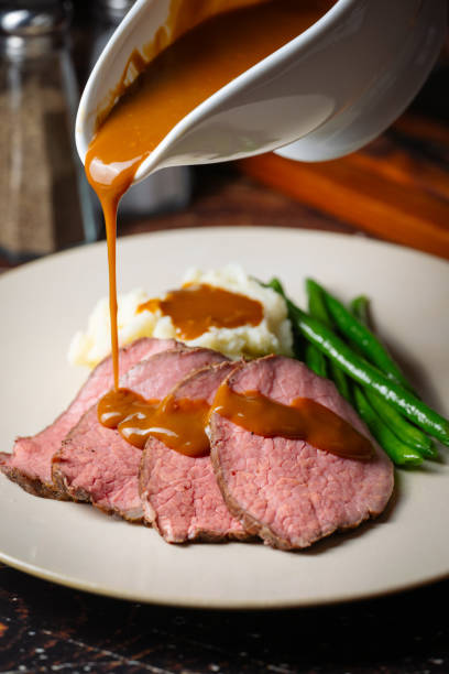 pouring brown gravy sauce on roasted beef