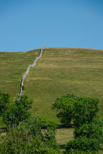 A long dry wall stretches across the hillside and divides the green pastures. Traditional stone fences, widely used throughout the English countryside, creating interesting patterns in the landscape.