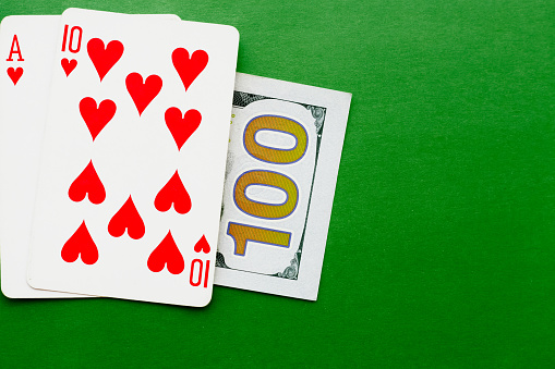 The ace of hearts and the ten of hearts lie on a hundred-dollar bill on a green background, playing blackjack in a casino, winning in a casino