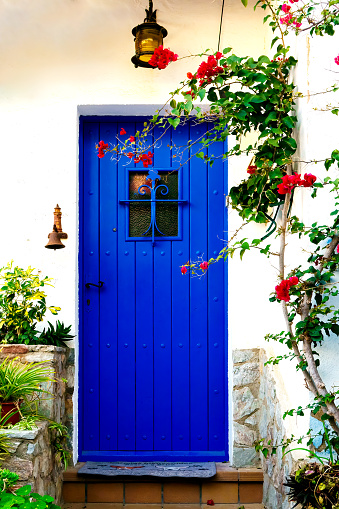 Blue door adorned with red flowers. Typical house of the villages of the Mediterranean coast on the Costa Brava, Catalonia, Spain.
