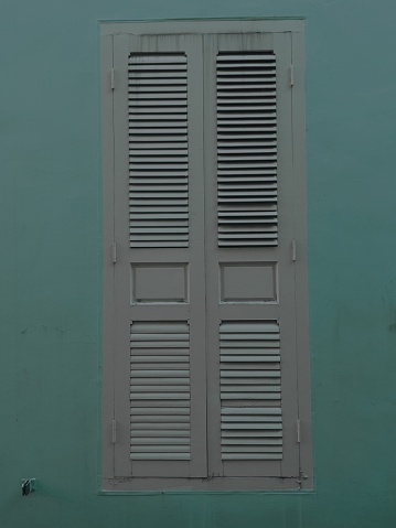 Vintage white wooden shutters on a pastel green wall, minimalist architectural detail.