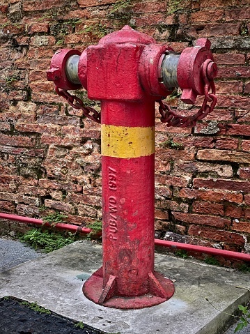 Vintage red and yellow fire hydrant against a weathered brick wall with visible textures and green moss.