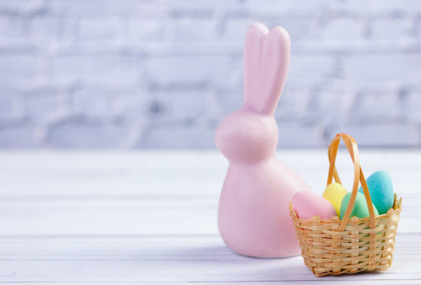 easter composition with a pink rabbit figurine and a basket with candies. - figurine easter egg easter holiday foto e immagini stock