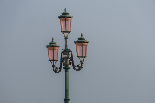 A street light lamp with pink colored glass in front of a hazy sky, Venice, Veneto, Italy