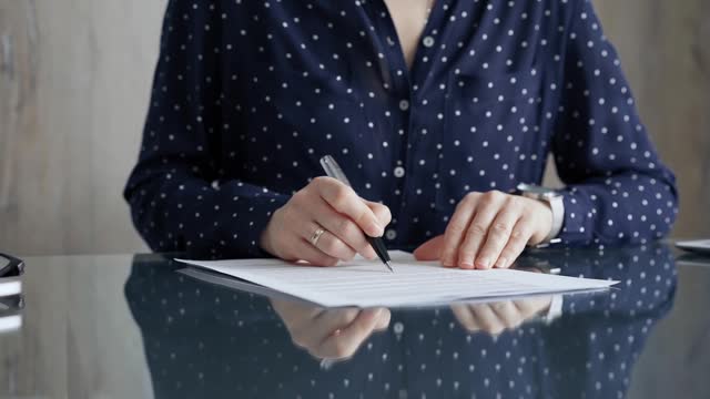 Businesswoman is signing corporate contract at her office desk in formal dark blue blouse with polka dots. Business people concept