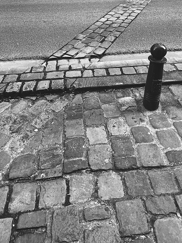Black and white image of a cobblestone street with a metal bollard. Vintage urban texture.