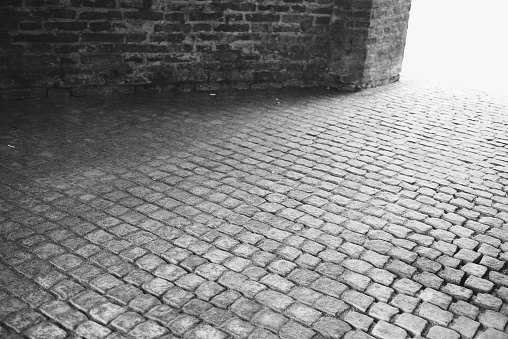 Old cobblestone street with brick wall, monochrome vintage texture.
