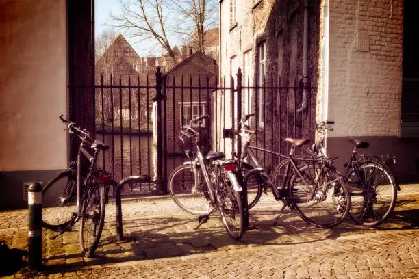 Vintage-style photo of bicycles parked against a metal fence on a cobblestone street, with old buildings in the background.