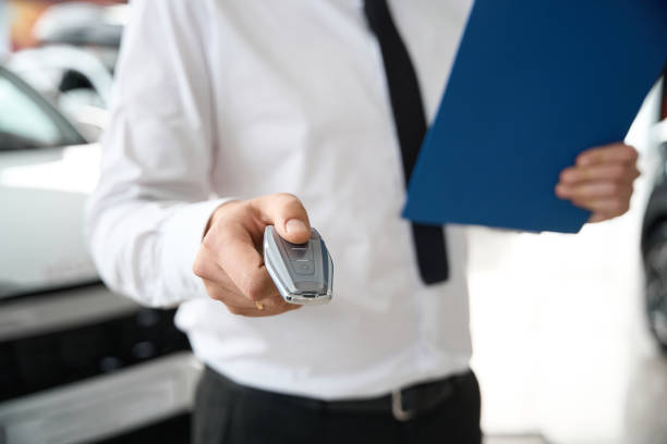 istock Man holding clipboard with documents and automobile keys in car dealership 2121219084