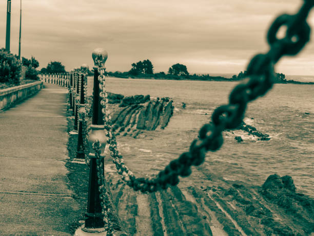 Chain and bollard barrier  around rocky foreshore in monochrome