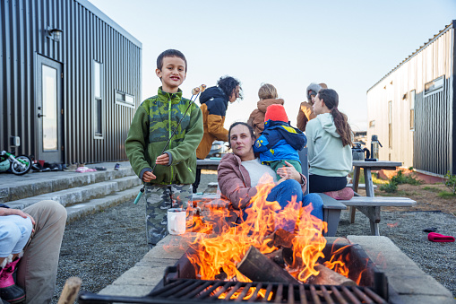 An adult woman and her children sit at a campfire pit with their extended family, roasting marshmallows during a winter vacation at the Oregon coast.
