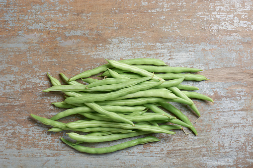 pile of green beans on wooden table top, aka string or snap beans or snaps, popular vegetable enjoyed for crisp texture, mild flavor and nutritional benefits, taken straight from above with copy space