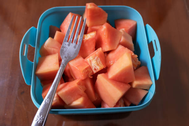 Ripe red papaya fruit that has been cut, with a fork in a purple box, on the table.