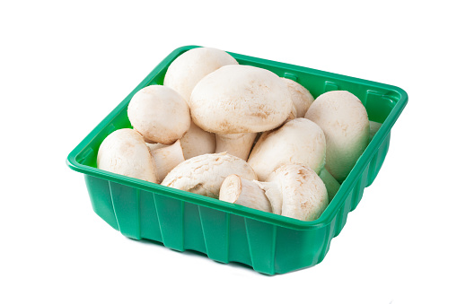 Raw mushrooms champignons set in a green plastic packaging on white background