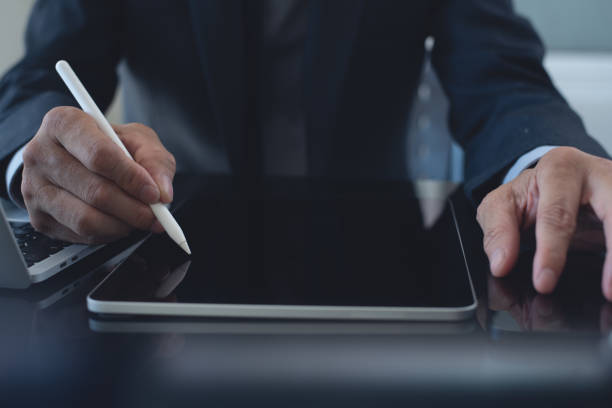 istock Businessman, manager working, using stylus pen signing e-document on digital tablet with laptop computer on table at modern office, e-signing, electronic signature, work planning, digital document concept 2121403299
