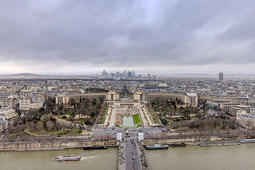 The views from the second floor of Eiffel Tower on a rainy and cloudy Christmas Day 2023, with cruise boat on Seine River in the front, Palais de Chaillot in the middle, and the high risers of La Defense in the back
