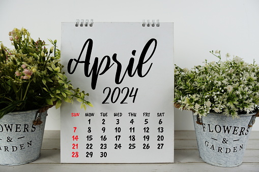 April 2024 monthly calendar with vintage alarm clock on wooden background