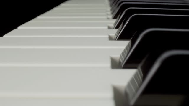 Camera moves over piano keyboard on black background. Closeup. Macro