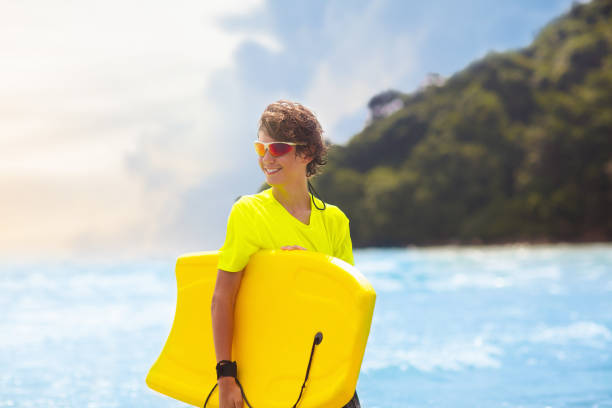 Teenage boy surfing on tropical beach. Family summer vacation in Asia. Kids swim in ocean water. Teenager on surf body board. Young adult swimming in exotic sea. Active water and beach sport.