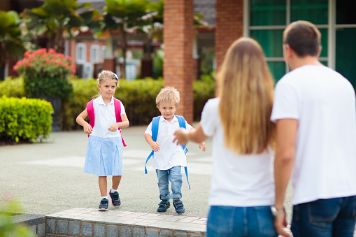 Mother and kids after school. Young mom picking up children after lessons in kindergarten or preschool. Pick up students. Boy and girl running to parents in school yard.