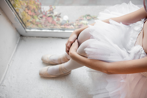 Close up ballet pointe shoes. Ballerina dancer sits by the window, pose relaxed, with pointe shoes on and the soft tulle of tutu, evoking moment of tranquility.