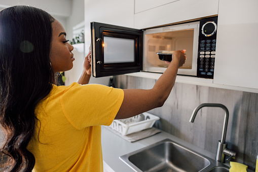A woman in the kitchen preparing herself lunch putting a bowl into the microwave.