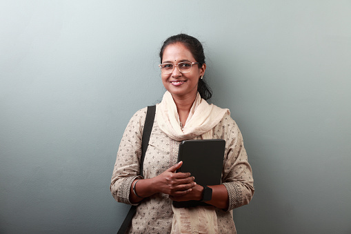 Woman of Indian ethnicity with a smiling face holding a tablet computer in hand