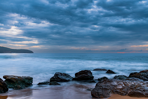 Cloudy sunrise seascape with waves and rocks at Killcare Beach on the Central Coast, NSW, Australia.