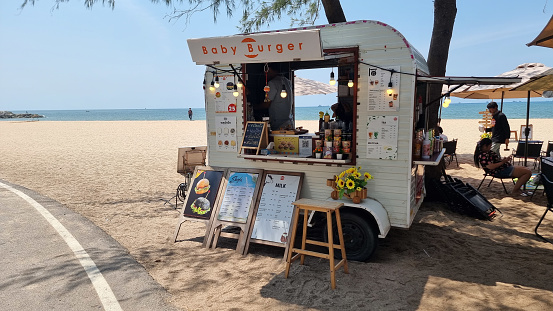 Rayong Thailand 13 March 2024, A vibrant food truck is parked on the sandy shore of a beach, serving up delicious dishes to beachgoers under a clear blue sky.