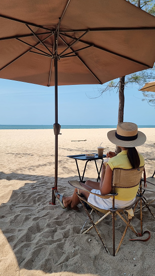 Rayong Thailand 13 March 2024, A woman relaxes in a chair under an umbrella on the sandy beach, enjoying the peaceful ambiance of the ocean waves.