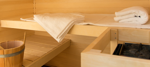 A small sauna with 2 wooden loungers. Small cabin in a bathroom. Sauna heater, loungers, water, towels