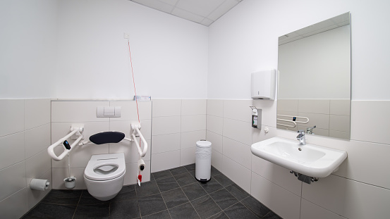 Disabled toilet with emergency alarm, armrest and space for wheelchairs. Wide angle perspective.