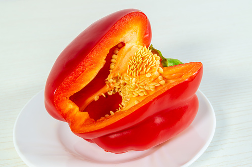 A red pepper is cut in half and placed on a white plate. Concept of freshness and healthiness, as the bright red color of the pepper is visually appealing and suggests that it is a nutritious food