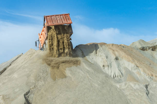 Dump truck with the tailgate open unloading sand at the top of a storage pile, low angle view.