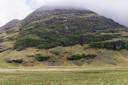 Majestic mountain draped in greenery under a cloud-capped peak, as viewed from the lush valleys near Glen Coe, offering a sense of the Scottish Highlands wild grandeur