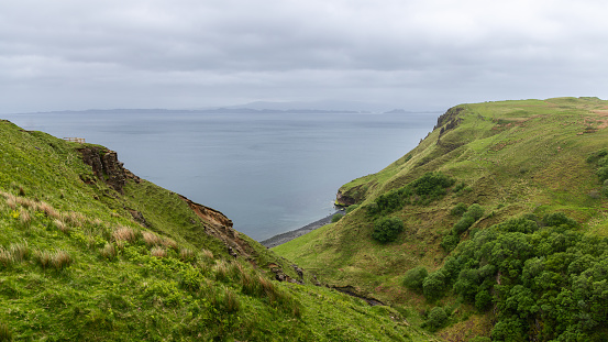 The lush green cliffs of the Isle of Skye overlook the calm sea, with a viewing platform inviting onlookers to take in the expansive coastal panorama