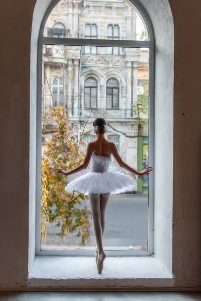istock Ballerina poses en pointe, white tutu within an arched window frame, juxtaposing the refined beauty 2121974302